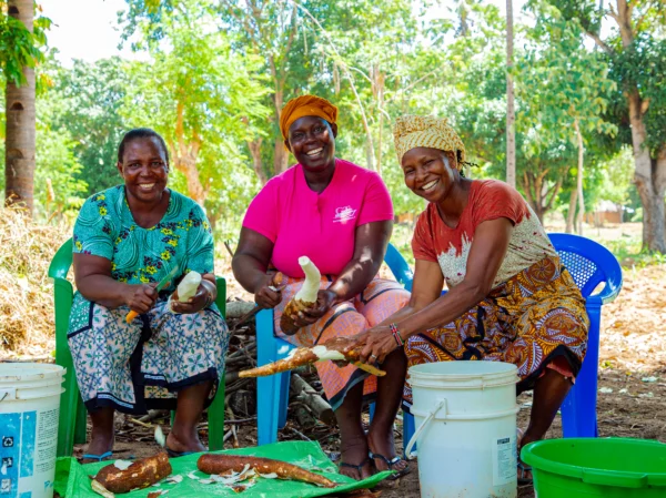 Three women smiling as they peel and process cassava at a rural development project in Tanzania